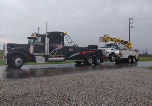 Black wrecker towing a utility truck, part of Heartland's Towing Service for Mattoon IL